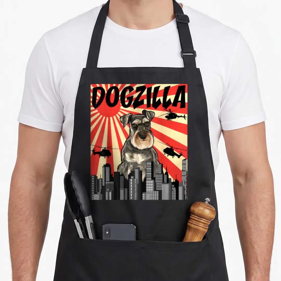 Japanese miniature schnauzer apron - Giant grey dog DOGZILLA behind city skyline with helicopters on red sunburst — shown on a black cotton canvas apron against a white background