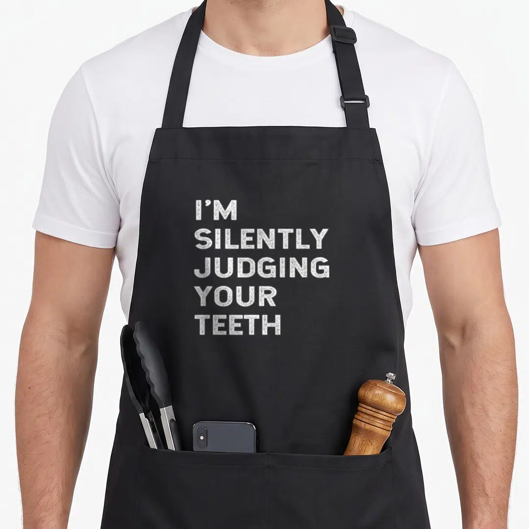 Silently dentist apron - White stacked text I'M SILENTLY JUDGING YOUR TEETH on black background — shown on a black cotton canvas apron against a white background