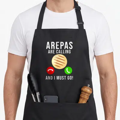 Arepas food aprons - Cartoon arepa between red and green phone buttons with white text — shown on a black cotton canvas apron against a white background