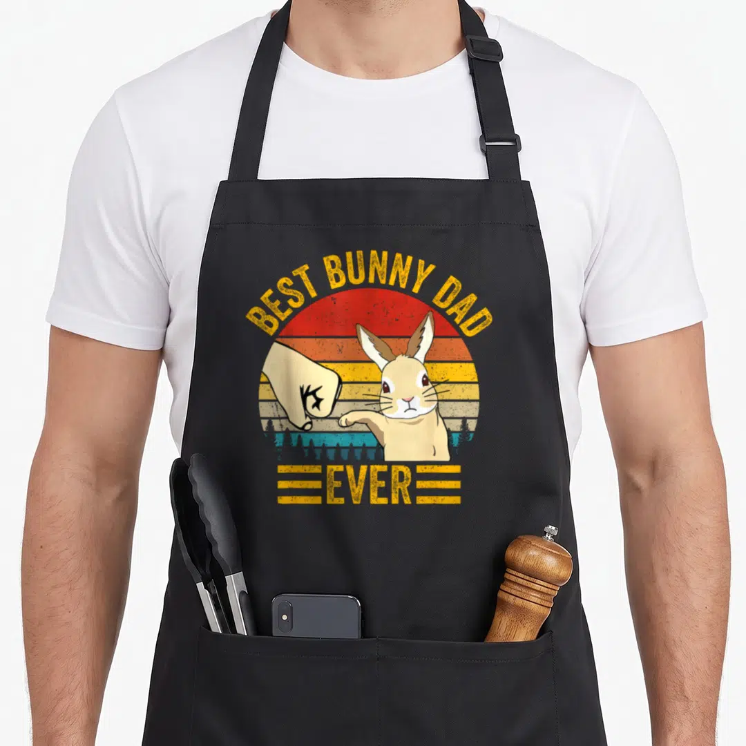 Father bunny apron - Best Bunny Dad Ever text with cartoon bunny fist bumping hand over retro sunset — shown on a black cotton canvas apron against a white background