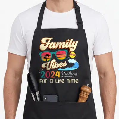 Family reunion memory apron - Retro Family Vibes 2024 text with teal sunglasses reflecting palm trees and a smiling sun — shown on a black cotton canvas apron against a white background