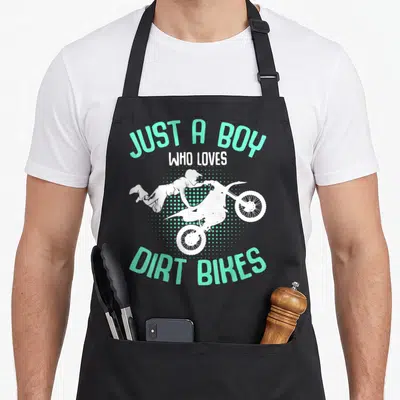 Enduro biking bike apron - JUST A BOY WHO LOVES DIRT BIKES text with white rider silhouette over mint green halftone — shown on a black cotton canvas apron against a white background