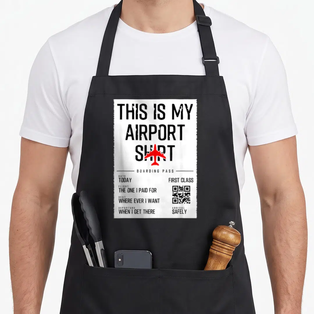 Airport travel aprons - Boarding pass style apron with red airplane and text reading This Is My Airport Shirt First — shown on a black cotton canvas apron against a white background