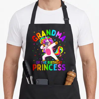 Dabbing grandma in apron - Rainbow unicorn dabbing with GRANDMA OF THE BIRTHDAY PRINCESS text and scattered hearts — shown on a black cotton canvas apron against a white background