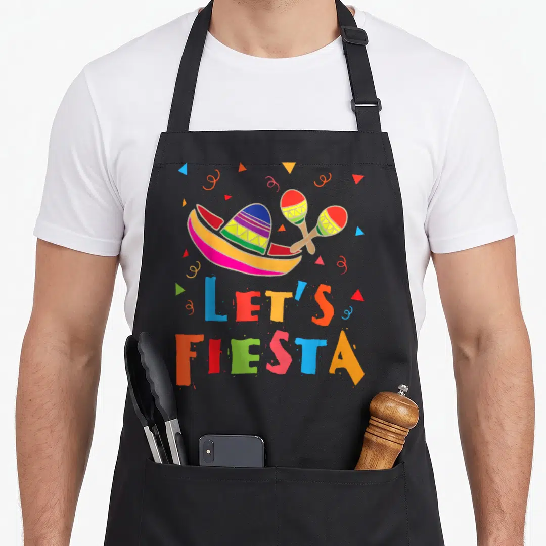 Fiesta mexico apron - Sombrero and maracas above multi-colored LET'S FIESTA text with confetti triangles — shown on a black cotton canvas apron against a white background