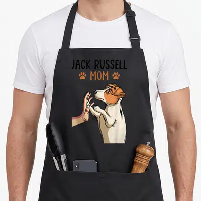 Jack dog dad apron - JACK RUSSELL MOM text with orange paw prints and a terrier high-fiving a hand — shown on a black cotton canvas apron against a white background