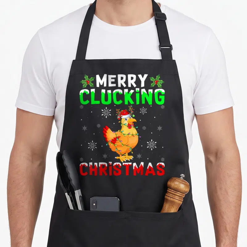 Clucking merry christmas apron - Cartoon chicken in Santa hat wrapped in lights with Merry Clucking Christmas text — shown on a black cotton canvas apron against a white background