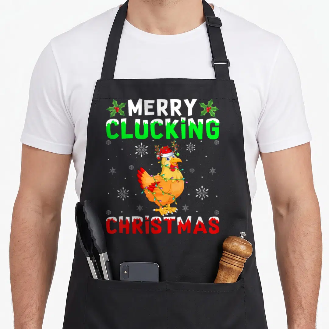 Clucking merry christmas apron - Cartoon chicken in Santa hat wrapped in lights with Merry Clucking Christmas text — shown on a black cotton canvas apron against a white background
