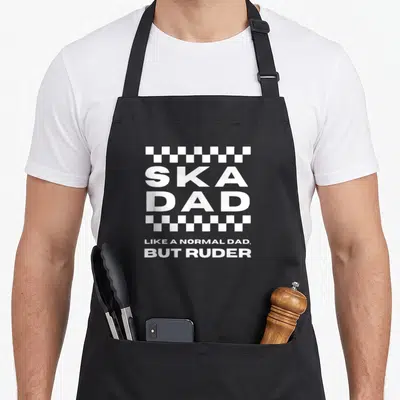 Normal ska apron - White SKA DAD text between checkerboard strips with bottom caption — shown on a black cotton canvas apron against a white background