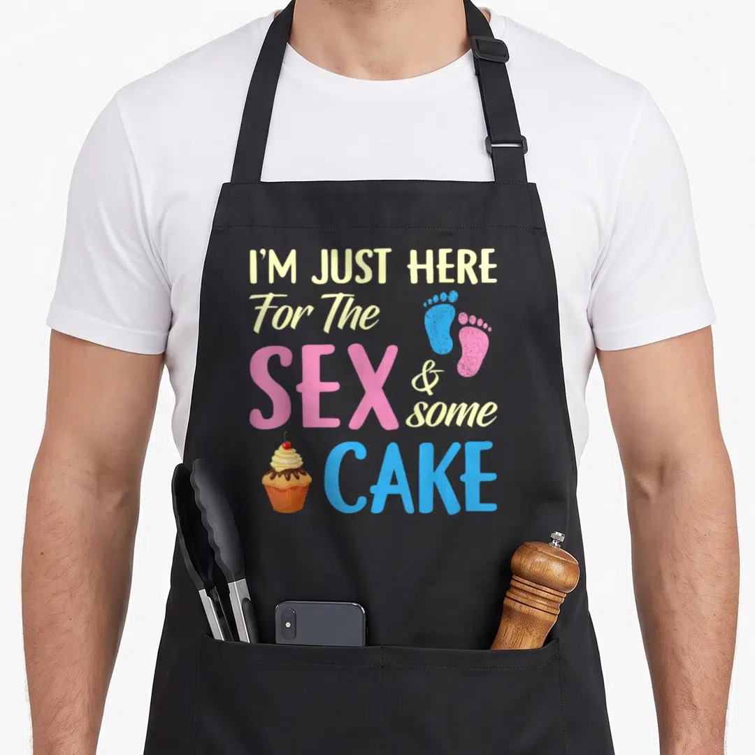 Gender cake apron - Stacked text I'M JUST HERE For The SEX & some CAKE with cupcake and blue pink footprints — shown on a black cotton canvas apron against a white background