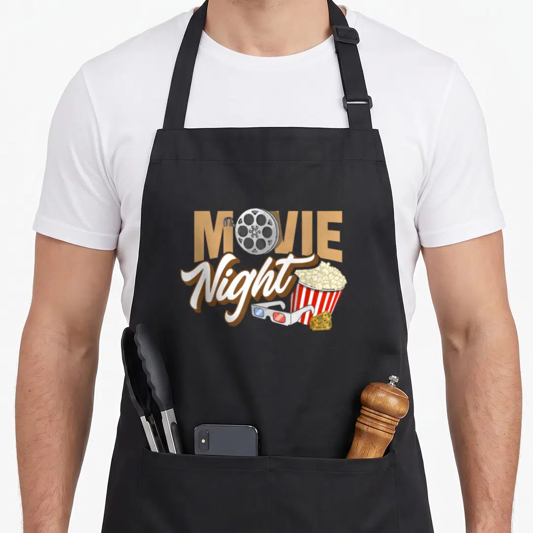 Night family aprons - MOVIE Night text with film reel, popcorn bucket, 3D glasses, and ticket in tan red white yellow — shown on a black cotton canvas apron against a white background