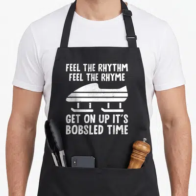 Feel bobsled apron - White distressed bobsled silhouette between text blocks reading FEEL THE RHYTHM FEEL THE RHYME GET — shown on a black cotton canvas apron against a white background