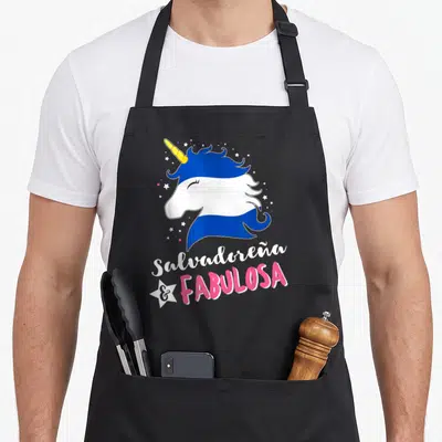 Unicornio salvadoran apron - Cartoon unicorn head in blue white pink with Salvadoreña and Fabulosa text and white star — shown on a black cotton canvas apron against a white background