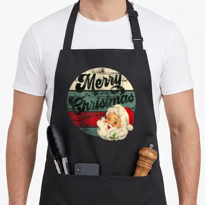 Santa old fashioned aprons - Retro Santa Claus head overlapping stacked Merry Christmas text on tri-color circle — shown on a black cotton canvas apron against a white background