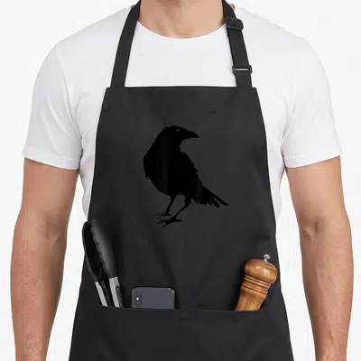 Beautiful bird aprons - Minimalist black crow silhouette standing in profile with visible eye and talons — shown on a black cotton canvas apron against a white background