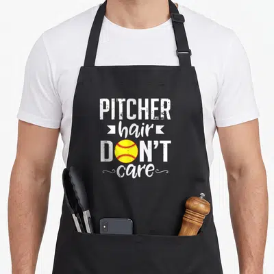Pitcher sports team aprons - Distressed text PITCHER hair DON'T care with yellow softball replacing O and white ribbons — shown on a black cotton canvas apron against a white background