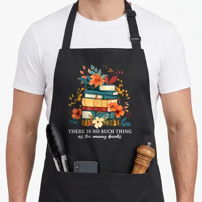 Librarian reading book apron - Stack of books surrounded by orange and blue flowers with white text saying THERE IS NO — shown on a black cotton canvas apron against a white background