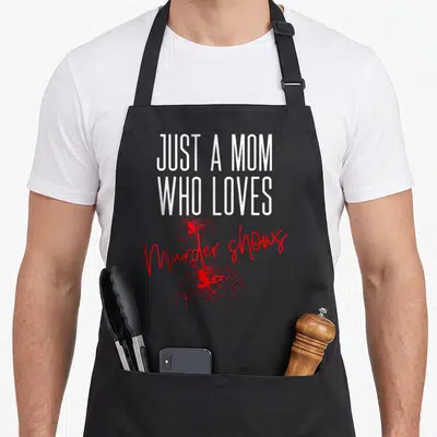 Murder detective apron - White text Just A Mom Who Loves above red script Murder Shows and blood splatter — shown on a black cotton canvas apron against a white background