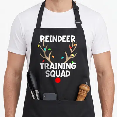 Running sports team aprons - REINDEER TRAINING SQUAD text with brown antlers wrapped in multicolored lights and a red — shown on a black cotton canvas apron against a white background