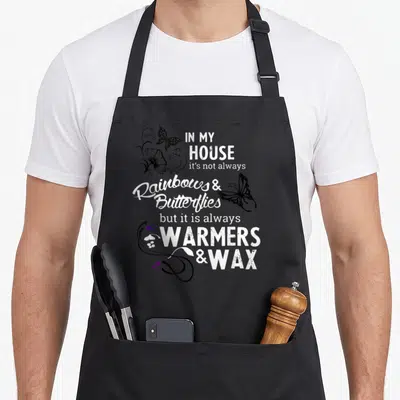 Warmer wax apron - Typography design reading WARMERS & WAX with butterflies and purple hearts — shown on a black cotton canvas apron against a white background
