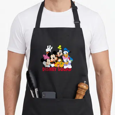 Funny squad friends apron - Disney characters group with DISNEY SQUAD text in red, yellow, blue, pink cartoon style — shown on a black cotton canvas apron against a white background
