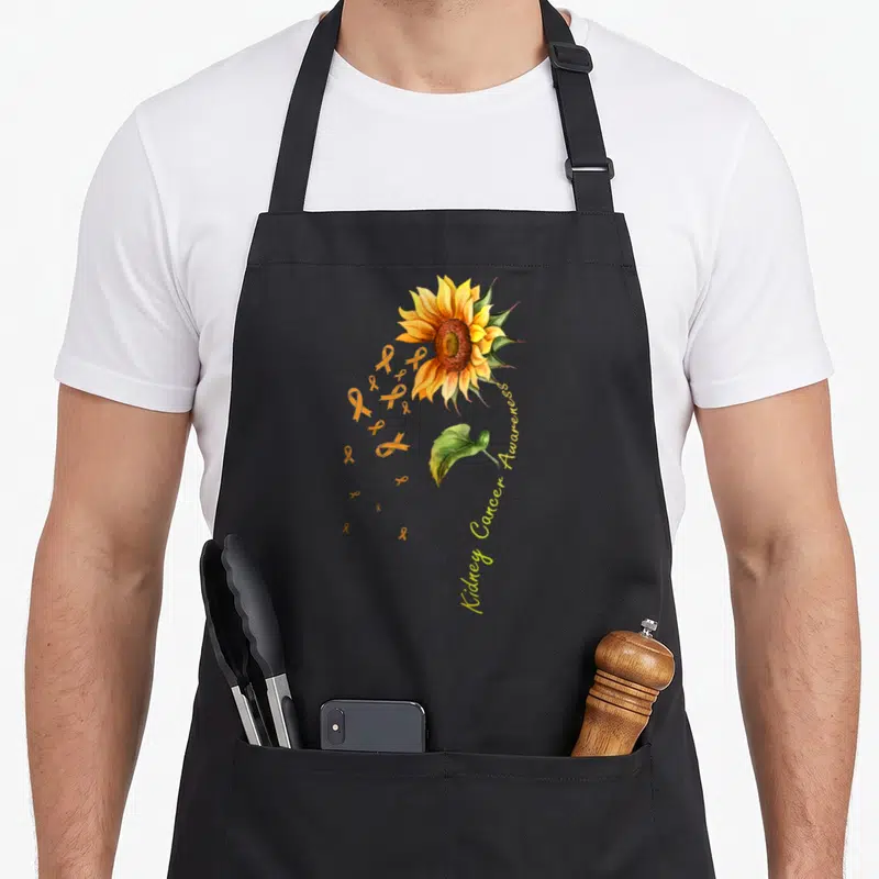 Kidney sunflower apron - Watercolor sunflower with orange ribbons and curved text reading Kidney Cancer Awareness — shown on a black cotton canvas apron against a white background
