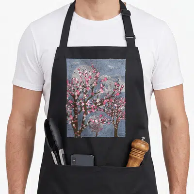 Japan cherry print apron - Watercolor cherry blossom trees with pink flowers, brown branches, and a large grey moon — shown on a black cotton canvas apron against a white background