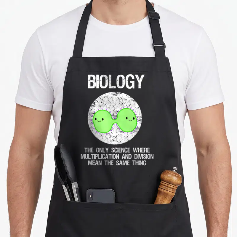 Funny biology teacher apron - BIOLOGY text above two dividing green bacteria in white circle with purple accents — shown on a black cotton canvas apron against a white background