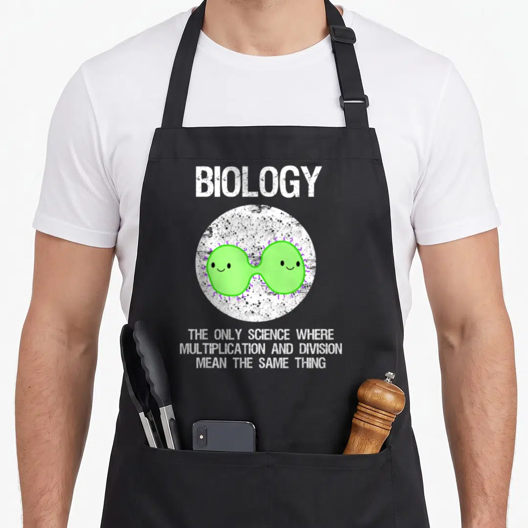 Funny biology teacher apron - BIOLOGY text above two dividing green bacteria in white circle with purple accents — shown on a black cotton canvas apron against a white background