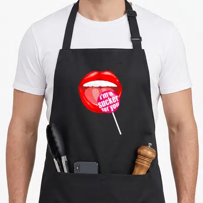Sucker candy aprons - Red cartoon mouth holding pink lollipop with white text i'm a sucker for you — shown on a black cotton canvas apron against a white background