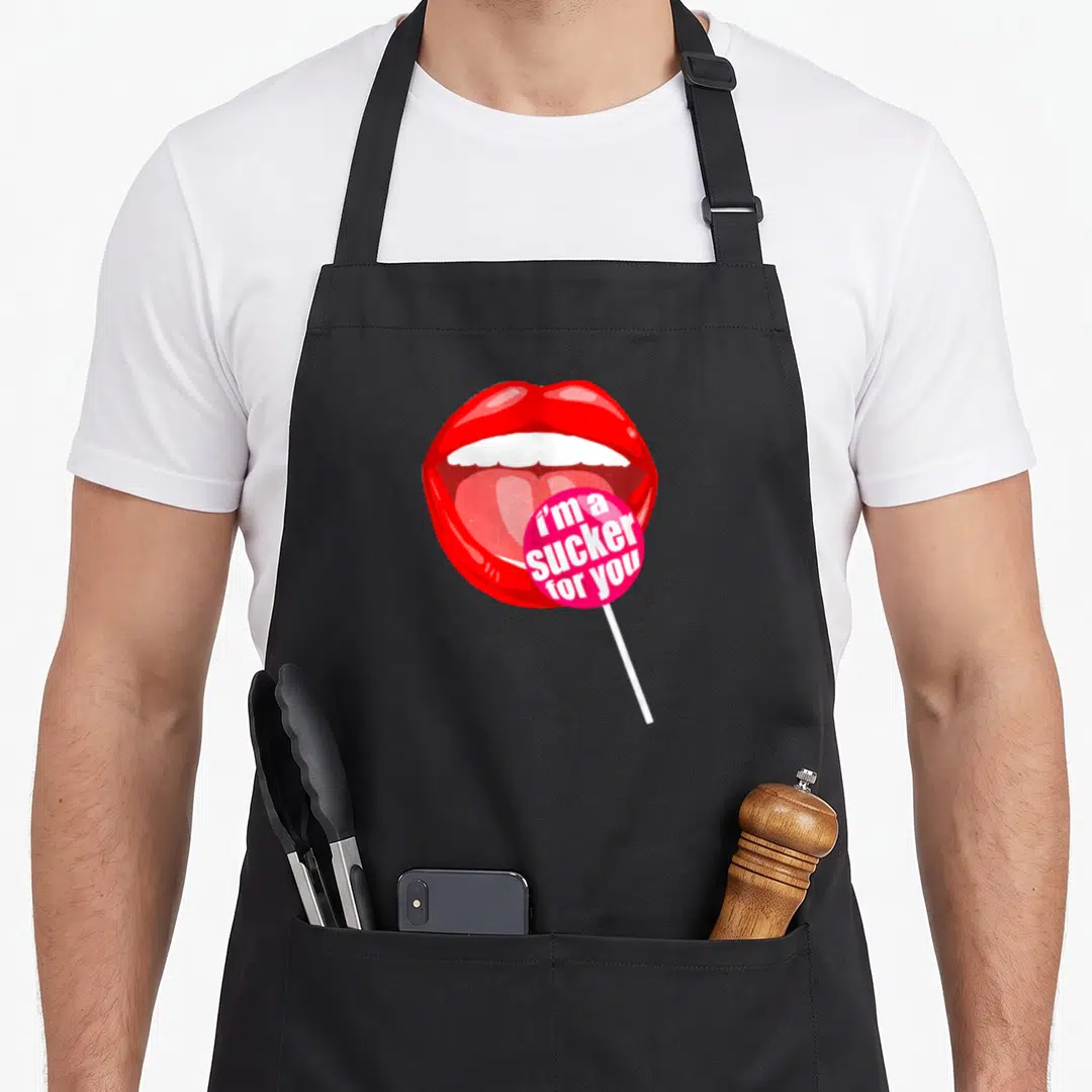 Sucker candy aprons - Red cartoon mouth holding pink lollipop with white text i'm a sucker for you — shown on a black cotton canvas apron against a white background