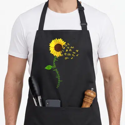 Occupational sunflower apron - Sunflower with occupational therapy text stem and orange activity icons — shown on a black cotton canvas apron against a white background