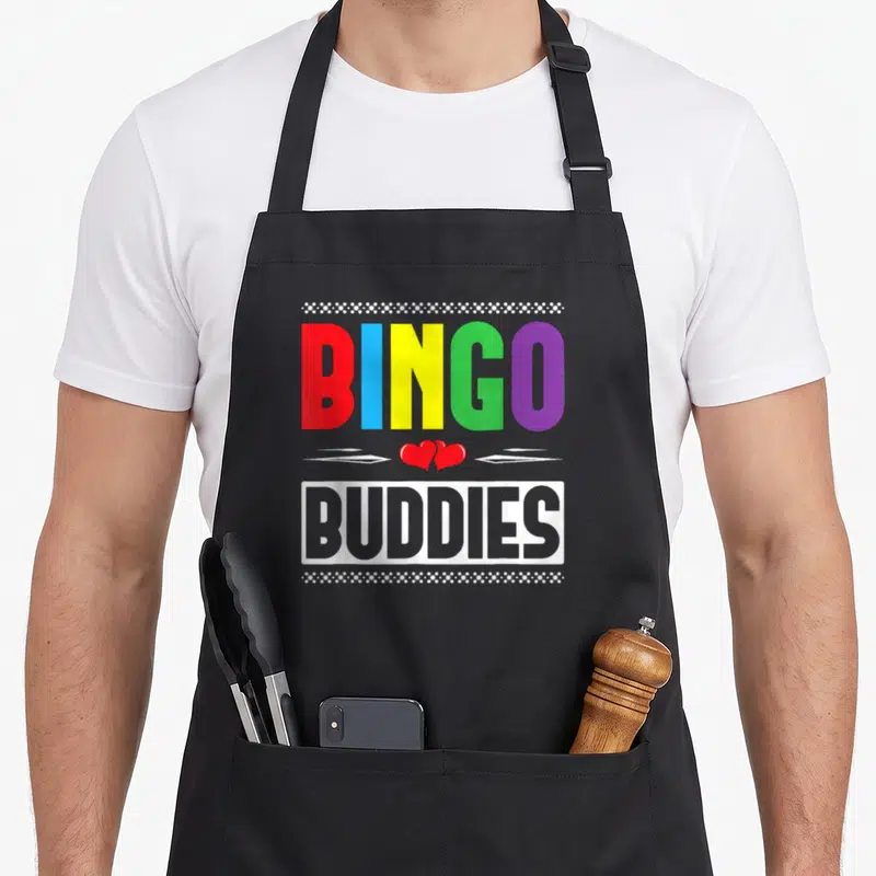 Buddy bingo apron - Rainbow BINGO BUDDIES text with two red hearts and white dotted borders — shown on a black cotton canvas apron against a white background