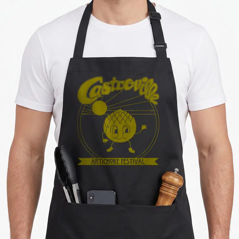 Dustin nerdy apron - Gold line art of Castcoville Artichoke Festival with walking artichoke character and sun — shown on a black cotton canvas apron against a white background