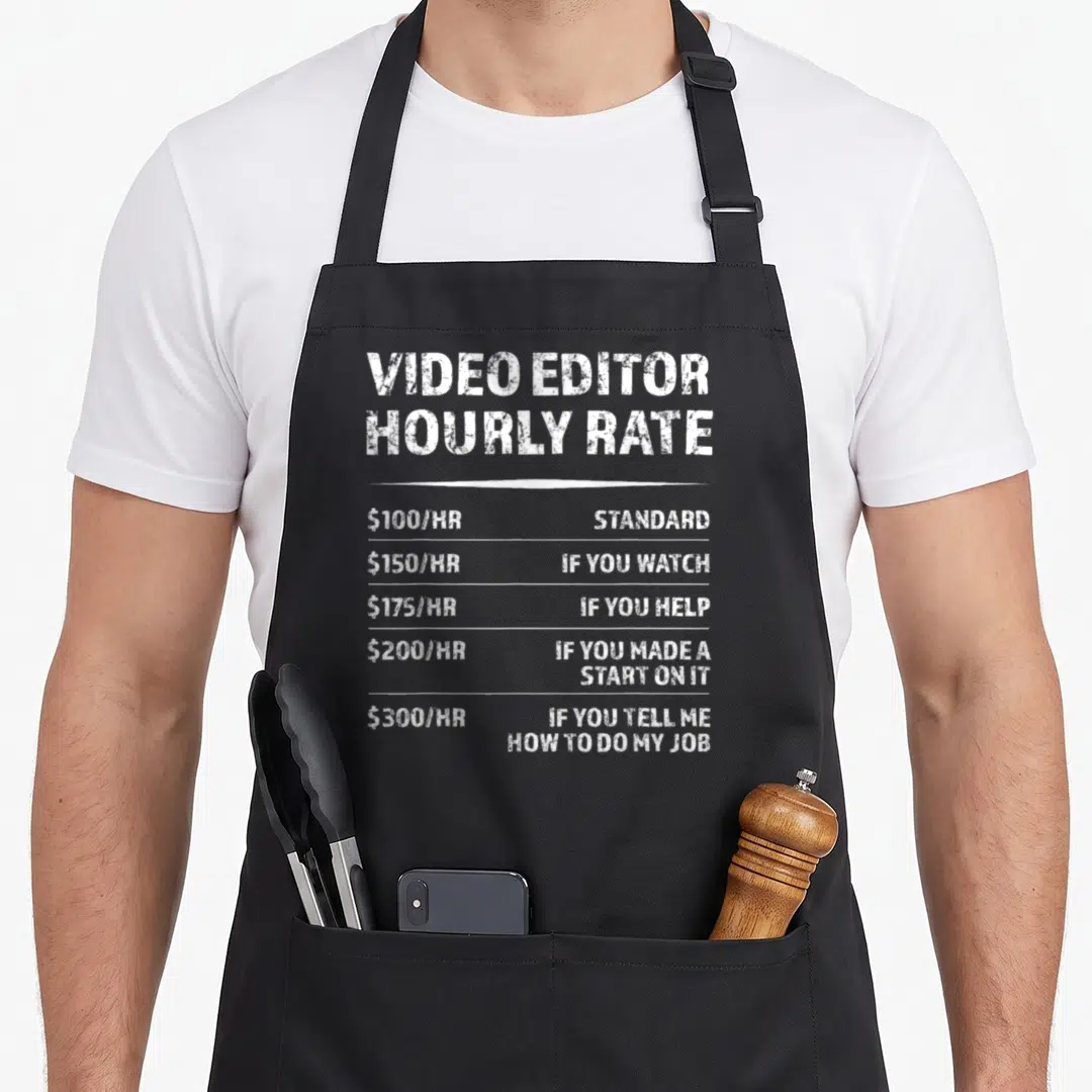 Editor videographer apron - White typography listing video editor hourly rates from 100 to 300 dollars per hour based — shown on a black cotton canvas apron against a white background