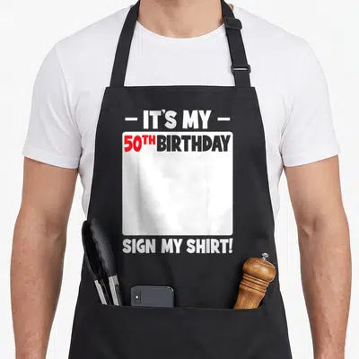 Cool 50th birthday apron - IT'S MY 50TH BIRTHDAY SIGN MY SHIRT text with white signing box — shown on a black cotton canvas apron against a white background