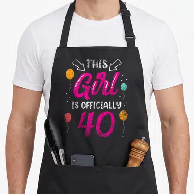 Officially age birthday apron - Stacked text This Girl Is Officially 40 with pink script, white block letters, and four — shown on a black cotton canvas apron against a white background