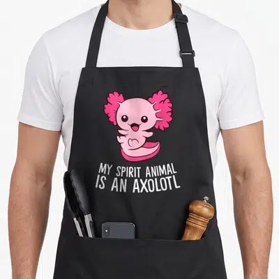 Pet axolotl animal apron - Pink cartoon axolotl with white text reading MY SPIRIT ANIMAL IS AN AXOLOTL — shown on a black cotton canvas apron against a white background