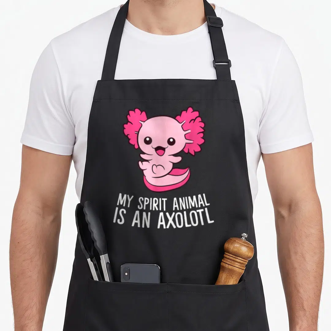 Pet axolotl animal apron - Pink cartoon axolotl with white text reading MY SPIRIT ANIMAL IS AN AXOLOTL — shown on a black cotton canvas apron against a white background