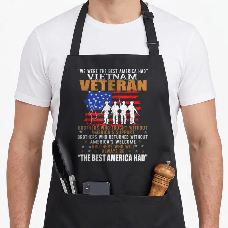 Vietnam who always apron - Four soldier silhouettes before distressed flag with We Were The Best America Had text — shown on a black cotton canvas apron against a white background