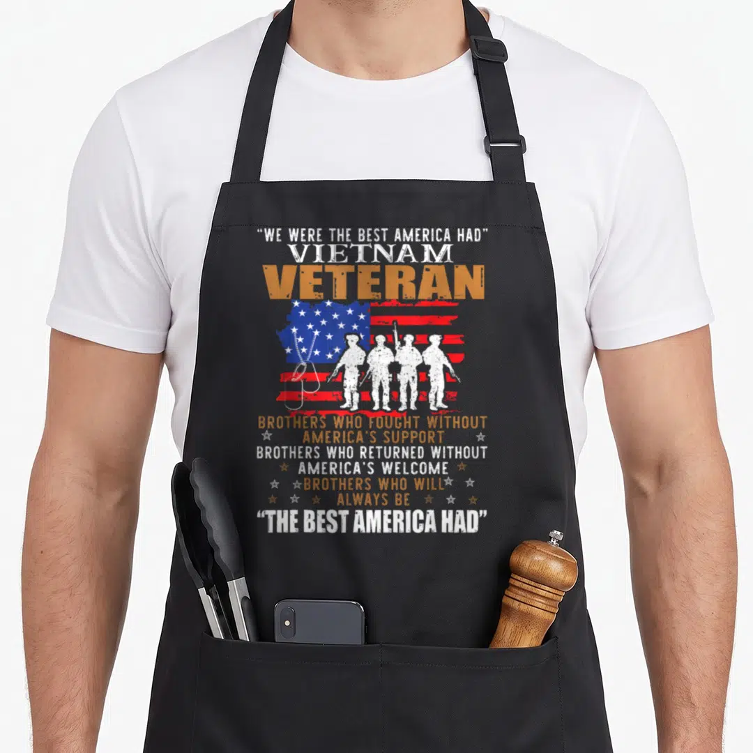 Vietnam who always apron - Four soldier silhouettes before distressed flag with We Were The Best America Had text — shown on a black cotton canvas apron against a white background