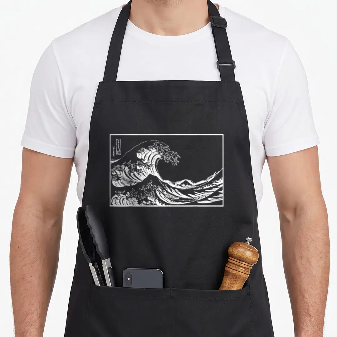 Wave outline of an apron - White line art of Great Wave off Kanagawa with mountain and boats inside rectangular frame — shown on a black cotton canvas apron against a white background