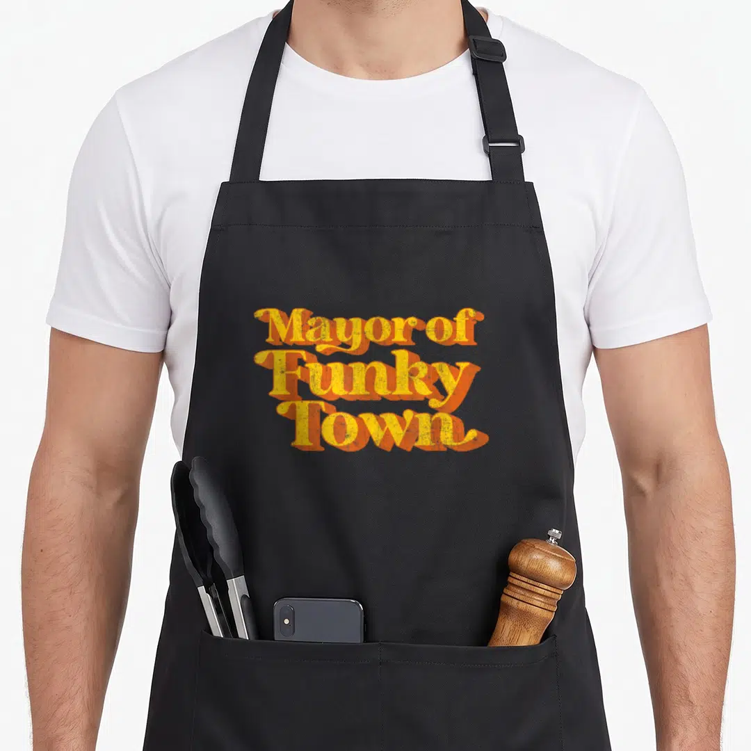 Mayor funky apron - Stacked yellow text Mayor of Funky Town with orange drop shadows — shown on a black cotton canvas apron against a white background