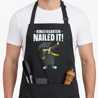 Dabbing nailed it aprons - Cartoon graduate dabbing holding diploma under stacked text with two stars — shown on a black cotton canvas apron against a white background