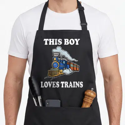 Wagon boy train apron - Cartoon blue steam train with THIS BOY LOVES TRAINS text in white — shown on a black cotton canvas apron against a white background