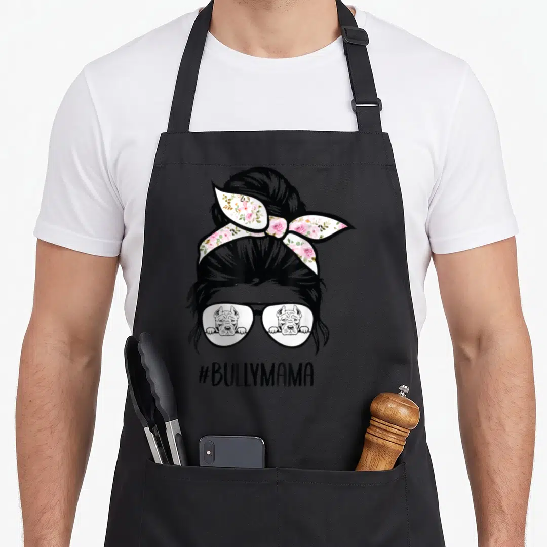 Bully messy aprons - Woman with messy bun and pink floral headband reflecting two dogs in sunglasses above #BULLYMAMA — shown on a black cotton canvas apron against a white background