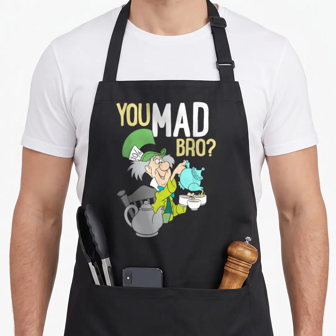 Mad alice wonderland apron - Mad Hatter pouring blue teapot next to YOU MAD BRO text in cartoon style — shown on a black cotton canvas apron against a white background