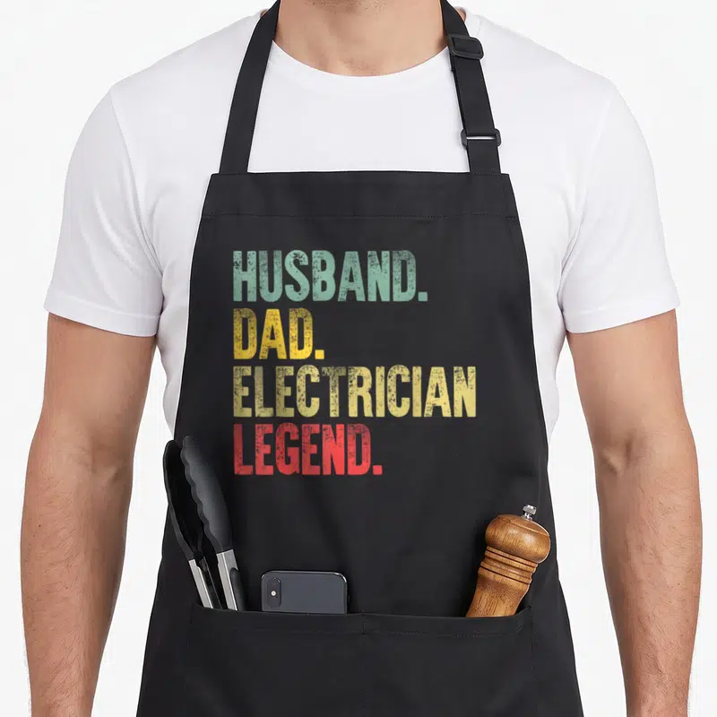 Legend electricians apron - Stacked HUSBAND. DAD. ELECTRICIAN. LEGEND. text in teal, yellow, and red distressed font — shown on a black cotton canvas apron against a white background
