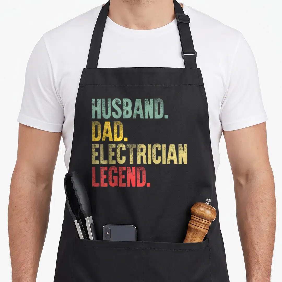 Legend electricians apron - Stacked HUSBAND. DAD. ELECTRICIAN. LEGEND. text in teal, yellow, and red distressed font — shown on a black cotton canvas apron against a white background