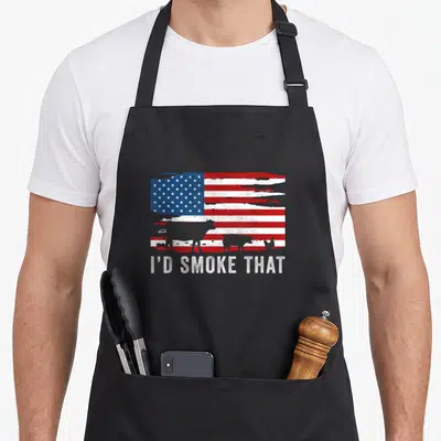 Vintage smoke barbecue apron - Distressed US flag with cow pig chicken silhouettes and I'D SMOKE THAT text — shown on a black cotton canvas apron against a white background